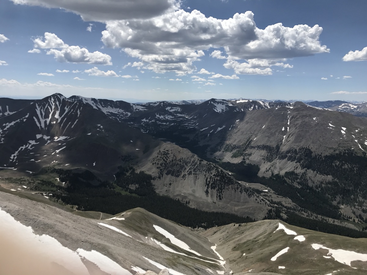 Snow-patched peaks and forested valleys of the Sawatch Range under cumulus clouds, seen from the summit of Mount Antero